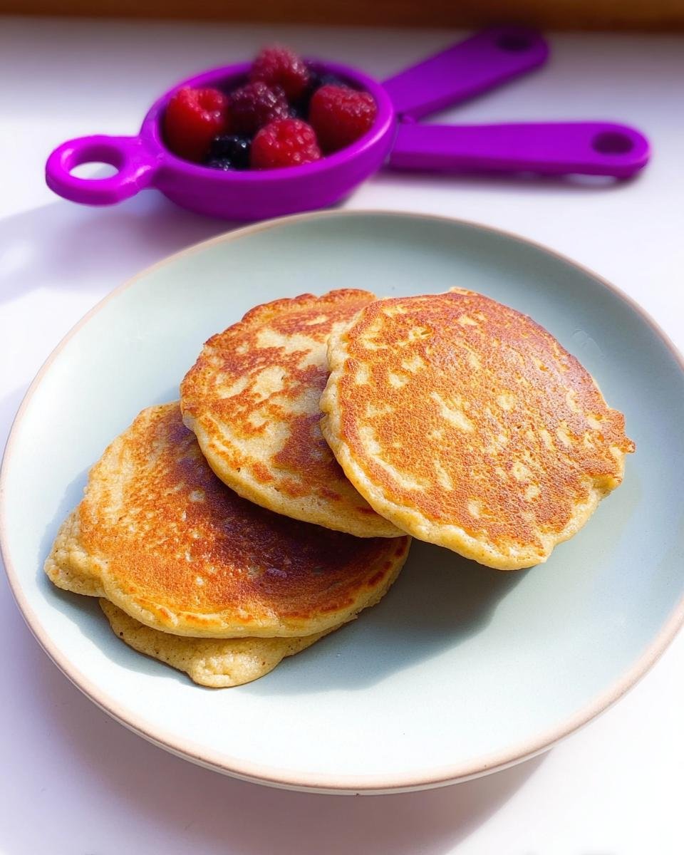A stack of three golden brown 3 Ingredient Banana Pancakes served on a light blue plate with berries in the background.