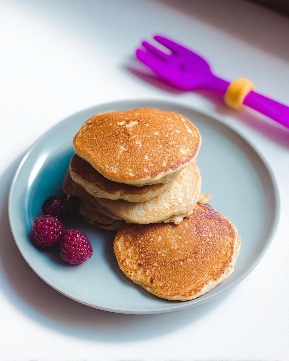 A stack of golden Three Ingredient Banana Pancakes served on a blue plate with fresh raspberries.