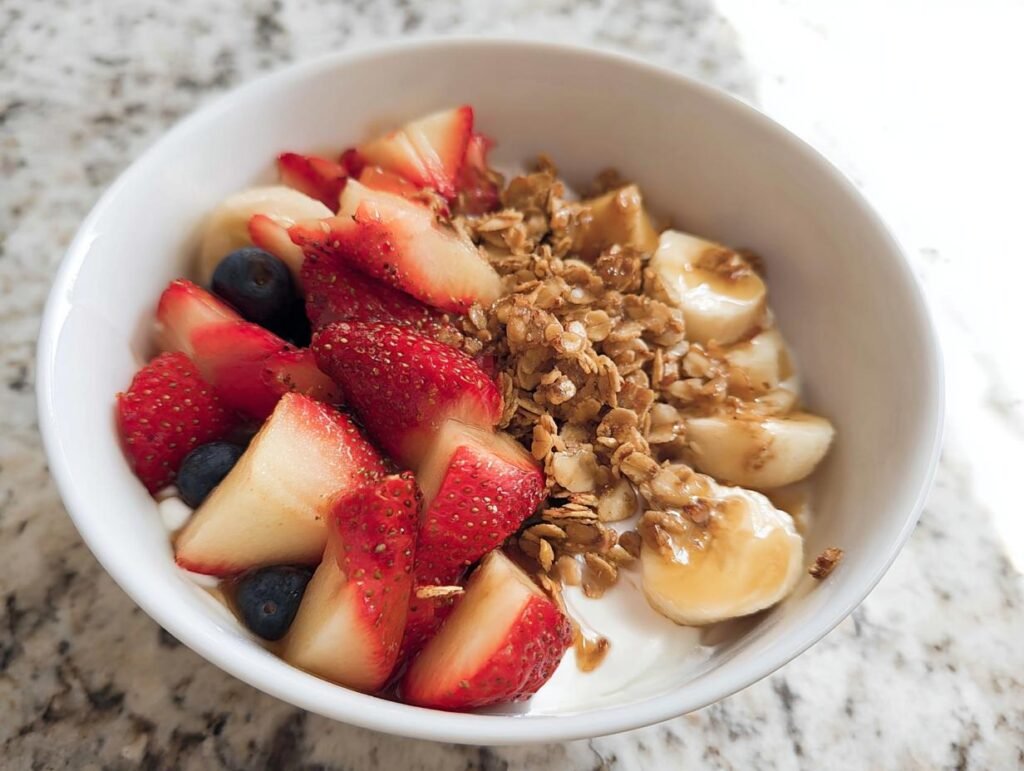 A vibrant Greek Yogurt Fruit Breakfast Bowl topped with fresh strawberries, blueberries, bananas, and crunchy granola.