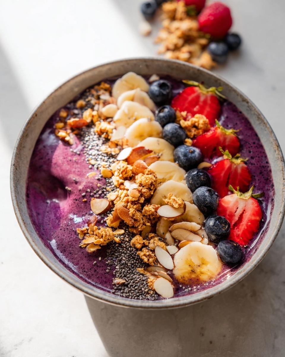 A vibrant Healthy Breakfast Smoothie Bowl topped with fresh banana slices, blueberries, strawberries, granola, chia seeds, and almonds.