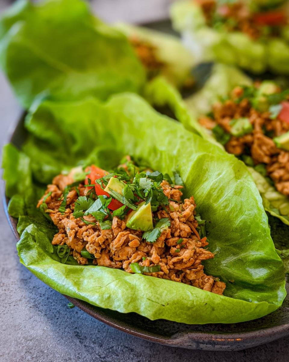 Close-up of healthy turkey lettuce wraps filled with seasoned ground turkey, topped with avocado, tomato, and cilantro.