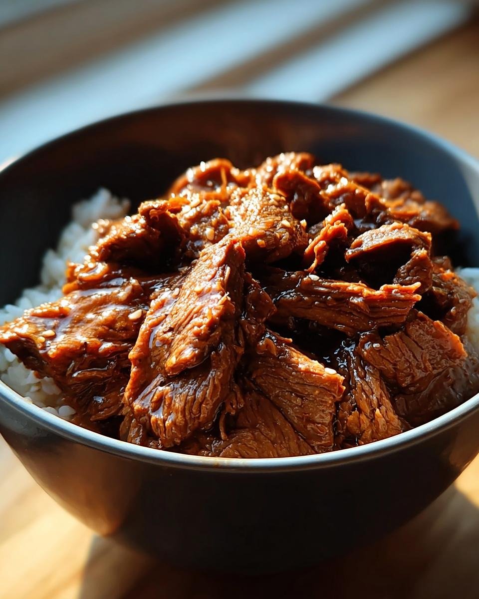 A close-up of a bowl filled with white rice and topped with tender, glazed Slow Cooker Korean Beef.